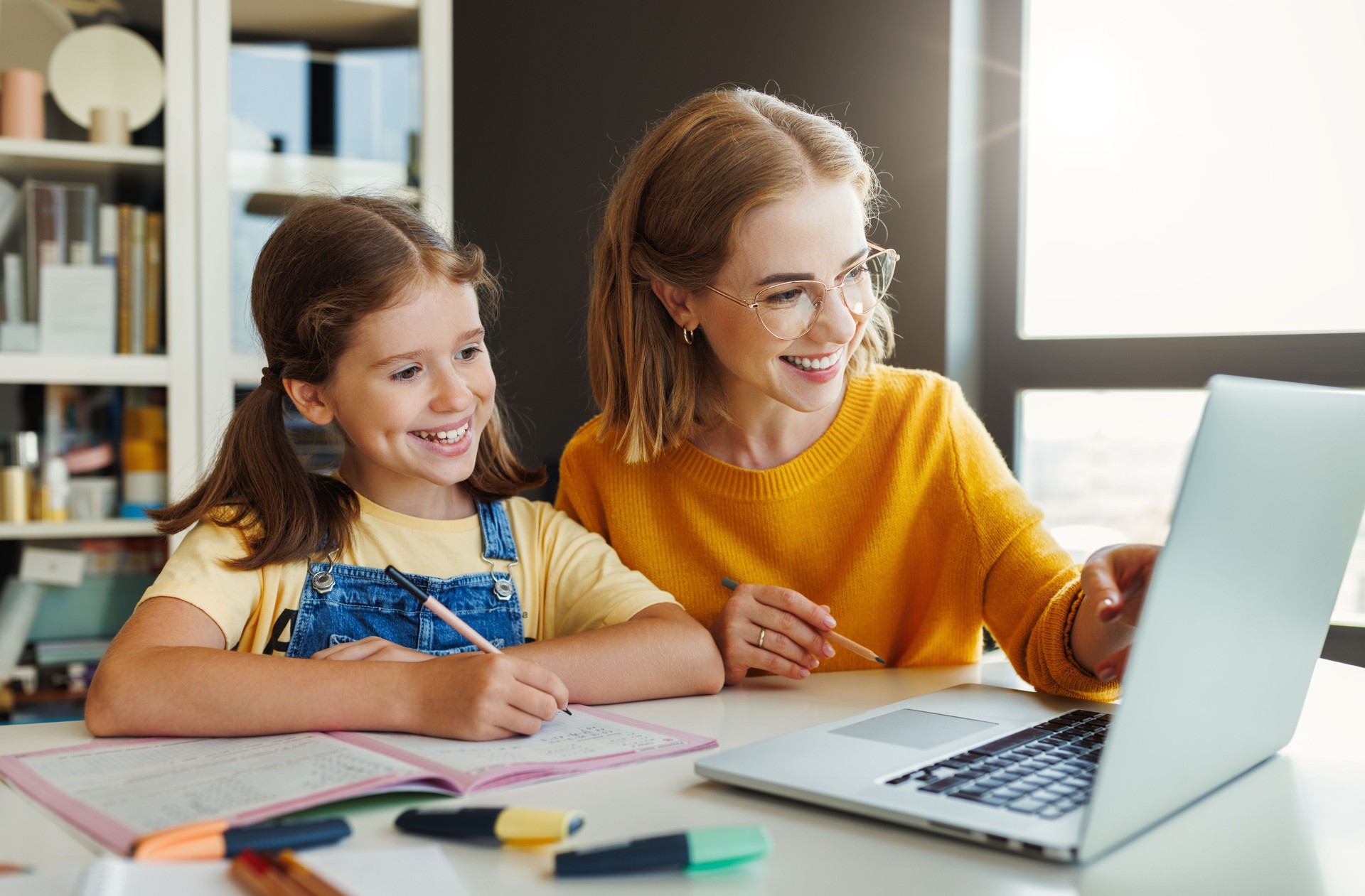 Cheerful mother doing homework with daughter at home